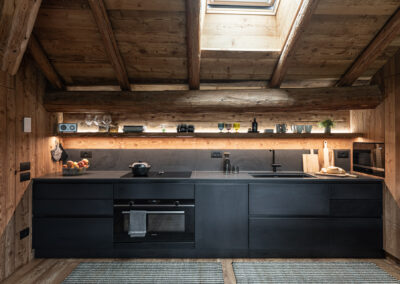 Cucina nera in legno e pietra con travi a vista, fotografia d’interni alpini in Val di Fiemme