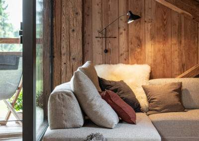 Living in legno con divano chiaro e luce naturale, fotografia d’interni alpini in Val di Fiemme